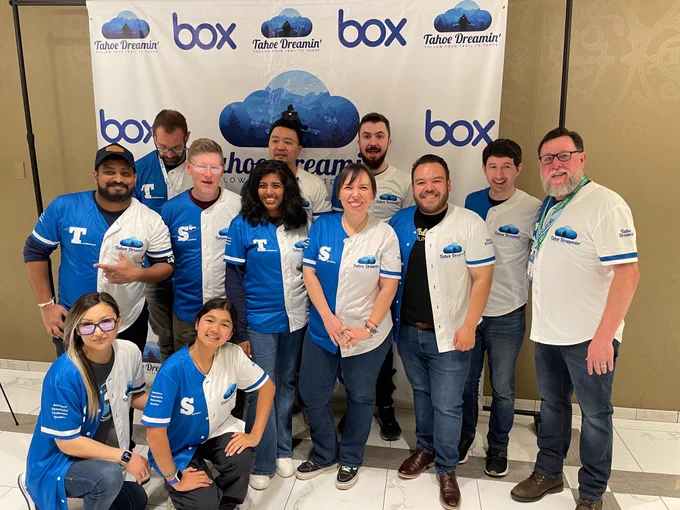 A group of attendees wearing blue and white Tahoe Dreamin’ baseball jerseys pose together in front of the event’s branded backdrop. Everyone is smiling, and the atmosphere is celebratory.