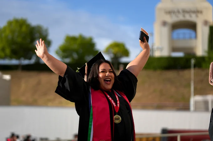 Graduate standing outside of the save mart center throws her arms out in celebration