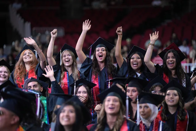 Graduates stand and cheer from their seats during commencement