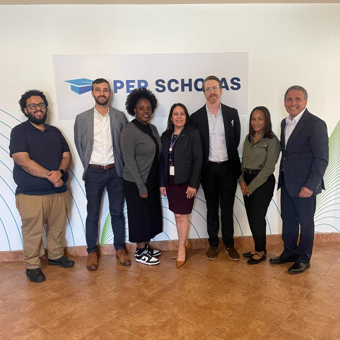 Members from Per Scholas including the President, and members from NYC Talent's Tech Talent Pipeline and Center for Youth Employment stand in front of the Per Scholas logo.