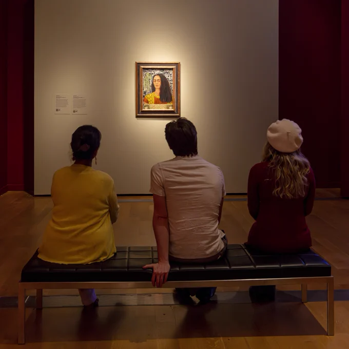 Three museum visitors sit and view a portrait of Frida Kahlo in VMFA's special exhibition "Frida: Beyond the Myth."