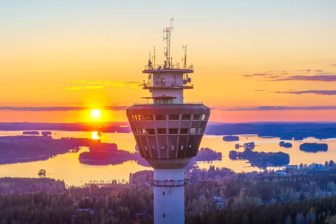 Puijon torni ja sen takana näkyy maisemassa laskeva aurinko, joka värjää maisemaa lämpimästi.