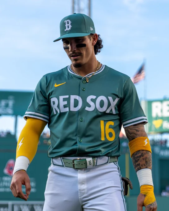Jarren Duran stands on the field at Fenway Park. He is wearing a green Red Sox City Connect jersey with white lettering, yellow numbering and a green cap.