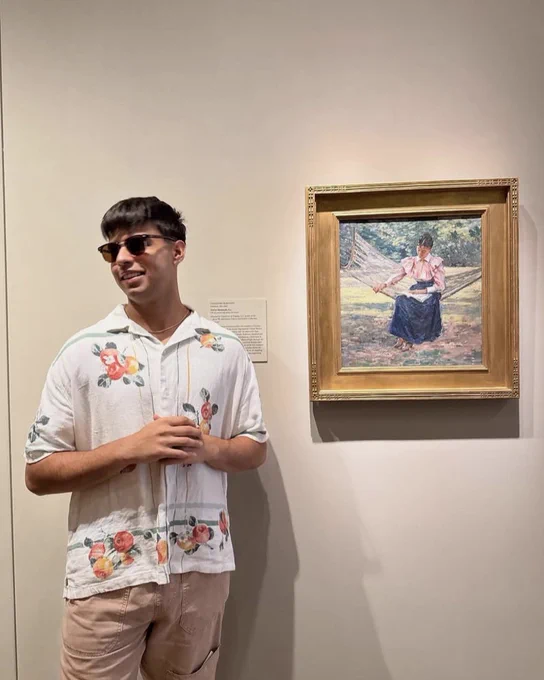 A museum visitor stands next to a painting of a person reading on a hammock in VMFA's American Art Galleries.
