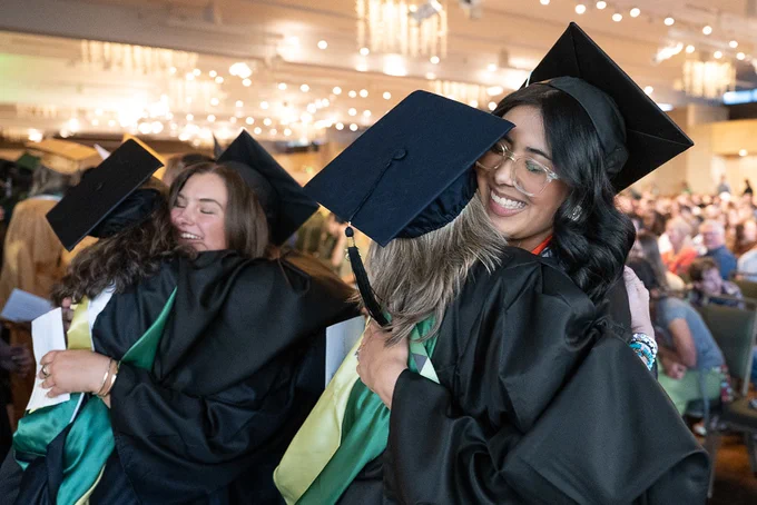 Two pairs of graduating students hugging during a recognition ceremony in the  L S C Ballroom.