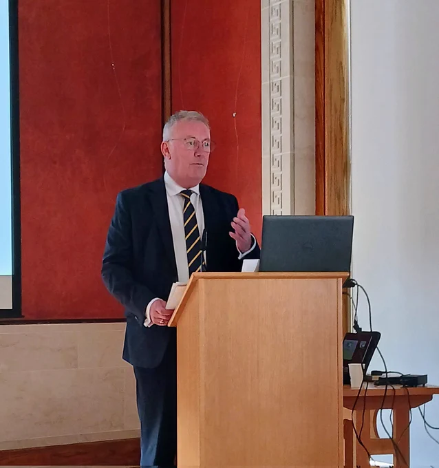 Health Minister Mike Nesbitt launching the NIABIF Event at Parliament Buildings. He is standing at a lecture in a sharp dark suit. His hand is raised and he is talking purposefully.