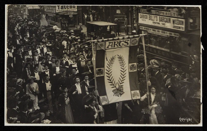 photograph 1909 suffrage procession many woment  graduates holng banner  with slogan arts walking down a street
