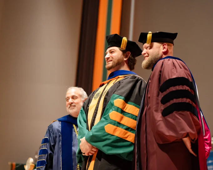 A grad poses for a photo after receiving a doctoral hood
