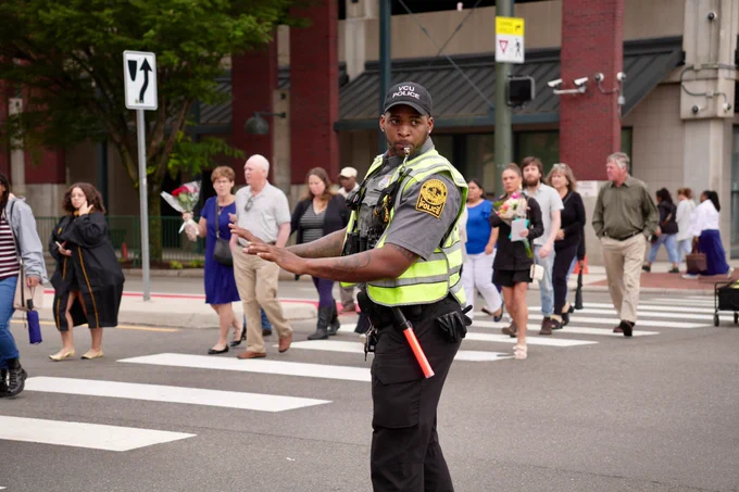 A VCU Police officer holds traffic while a group of pedestrians heading to a graduation ceremony crosses the street.