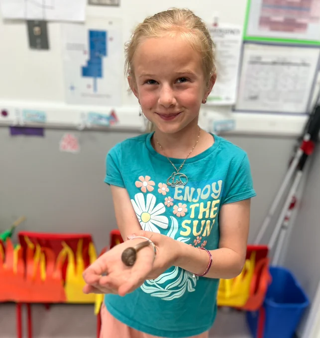 a girl with a fun graphic shirt holds her wrist, in her hand is a snail. 