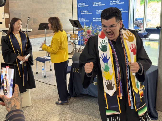  A graduate shows excitement by pumping their fists and giving a really big smile
