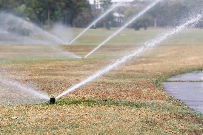 Sprinklers watering a grassy field with a path on the side.