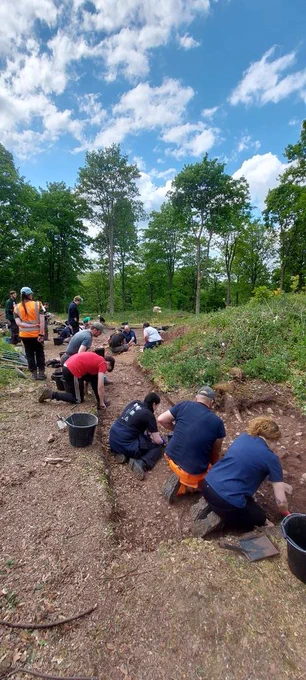 UCLan students at work cleaning trench under blue sky