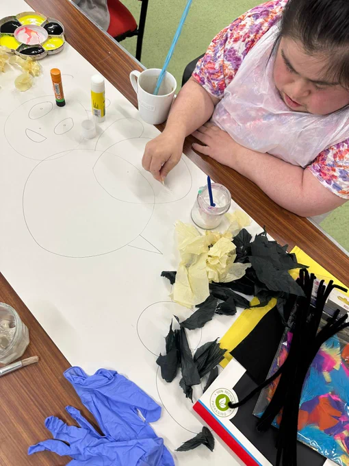 A young woman sat at a table using black and yellow tissue paper to make a bee collage. 