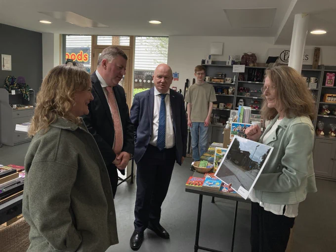 MSPs Colin Smyth and Gordon McDonald, and a Scottish Parliament staff member, are talking to the development officer at Alloa Hub - a community-owned and run facility providing services that benefit the residents and businesses of Clackmannanshire. They are being shown a photograph of the building before Alloa Hub took it over. 