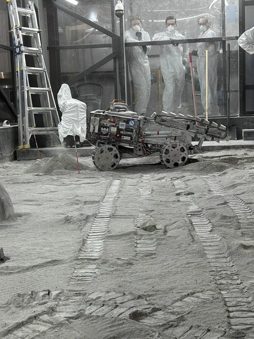 Meet ATLAS, the MTU MINE Astrohuskies' 2025 competition rover for the Lunabotics challenge. ATLAS stands for Advanced Terrain Lunar Alteration and Shaping rover. Photo shows the device scooping up simulated regolith ("moon dust") with a moveable conveyor of mini-buckets.