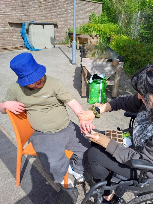 A young man wearing a blue bucket hat exploring some soil with his hands while a lady next to him plants seeds. 