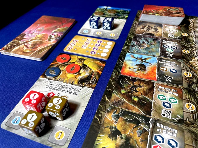 The edge of the board from the board game Shadow Kingdoms of Valeria. Atop the board are 'battle' cards and next to the board are 'great battle' cards.