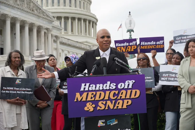 Rep. Ayanna Pressley stands behind a podium delivering remarks at a press conference on saving Medicaid and SNAP from Republican cuts.