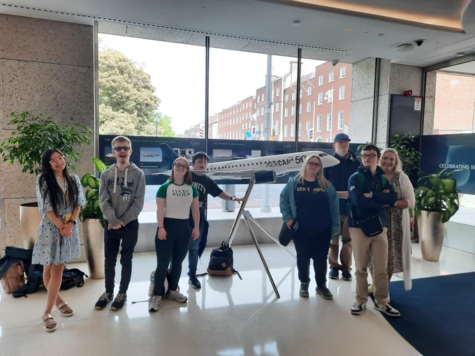A group of TCPID students standing in the lobby in AerCap with a large model aircraft with AerCap 50 written on it. 