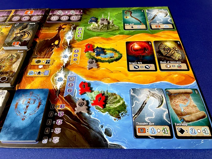 A game board from Shadow Kingdoms of Valeria with an extended board from the Riftlands expansion. Atop the board are cards with images of relics as well as some red, blue and gray tokens across the various landscapes.