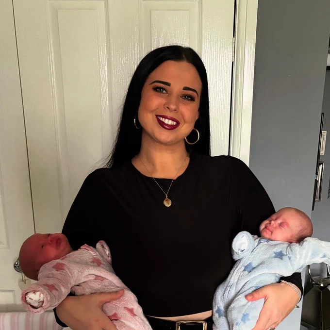 Person stands smiling holding new born twins