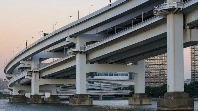 Curved split-level road bridge stands in water beside tall apartment buildings.