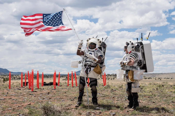 NASA astronaut Andre Douglas raises an American flag as NASA astronaut Kate Rubins looks on during their first simulated moonwalk in a week-long field test consisting of four simulated moonwalks and six advanced technology runs in the San Francisco Volcanic Field in Northern Arizona on May 13, 2024. Credit: NASA/Josh Valcarcel