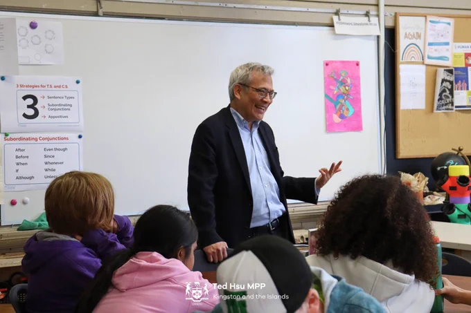 MPP Hsu standing smiling in front of a classroom of children.