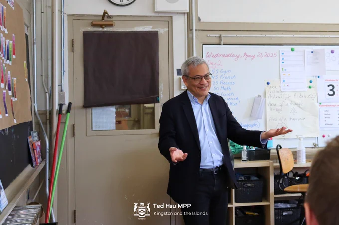 MPP Hsu walking into a classroom with his hands open and smiling.