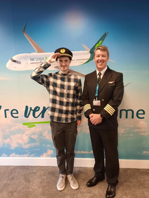 TCPID student Conor standing with an Aer Lingus pilot Stephen O'Reilly. Conor is wearing the pilot's cap and making a saluting sign. 