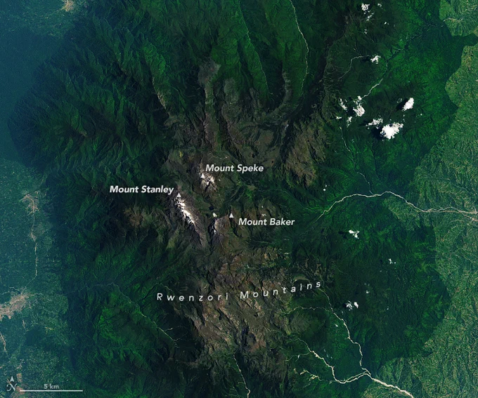 A detailed view of the Rwenzori Mountains, centered in the scene, shows the range's three highest mountains: Mount Stanley, Mount Speke, and Mount Baker. The peaks are topped with white, much of which is snow.