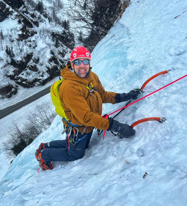 Erik ice climbing in Alaska with a yellow-orange winter coat and climbing gear on