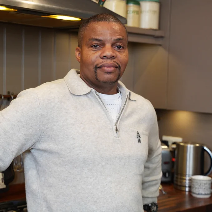 Peter wearing a grey sweater with a Prostate Cancer UK pin badge in a kitchen setting.