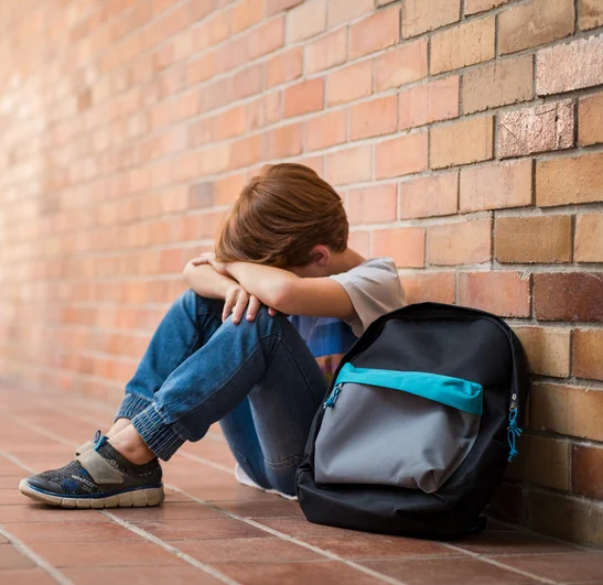 A young child sits against a brick wall, their head in their lap