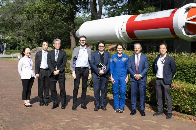 JAXA and ASA members stand outside at the JAXA Sagamihara Campus, in front of an M-series rocket. 