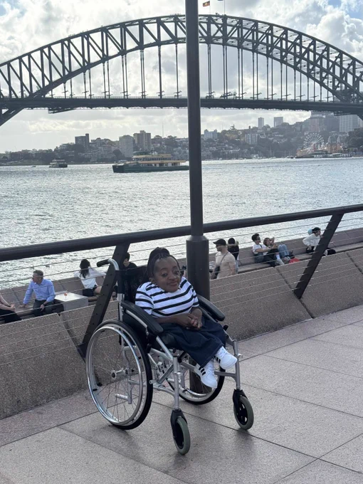 Australia Awards scholar, Florence, seated in her wheelchair with Sydney Harbour Bridge in the background.