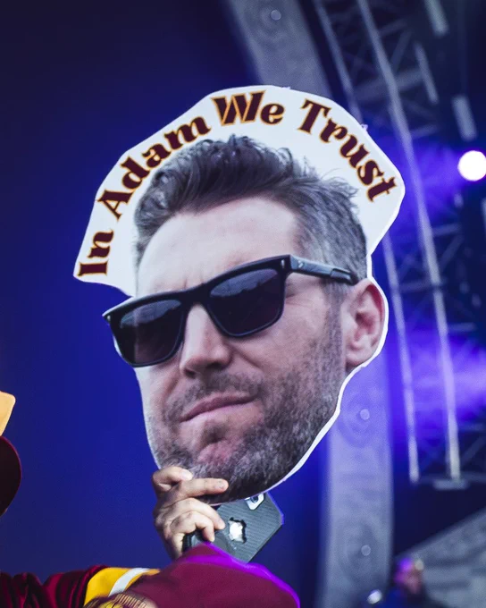 Photo of a poster from the 2024 NFL Draft in Detroit. The poster says "IN ADAM WE TRUST" with a photo of Adam Peters wearing sunglasses.