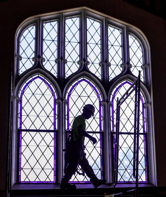 A construction working on the restoration of Hale Library silhouetted against the bright light filtering through a stained glass window.