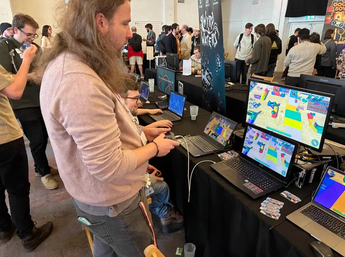 A focused player testing our Roblox game at GaMaYo 2025. The setup includes multiple laptops displaying vibrant game graphics, with other attendees exploring the event in the background.