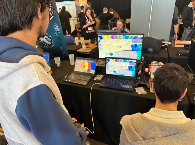 Two people playing our Roblox game at our demo booth at GaMaYo 2025. Multiple screens show colorful gameplay, capturing players fully immersed and engaged with the game.