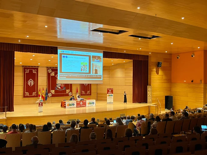 Imagen del auditorio durante la intervención de la ponente. Público sentado en la grada y el escenario al fondo con la mesa presidida por la ponente y el moderador.