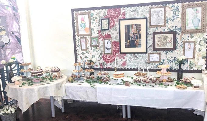 Tables with tablecloths and plates of food in the style of a Victorian tea room. Byrddau gyda lliain bwrdd a phlatiau o fwyd yn null ystafell de Fictoraidd.