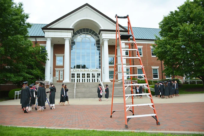 front of campus building with graduating seniors in front