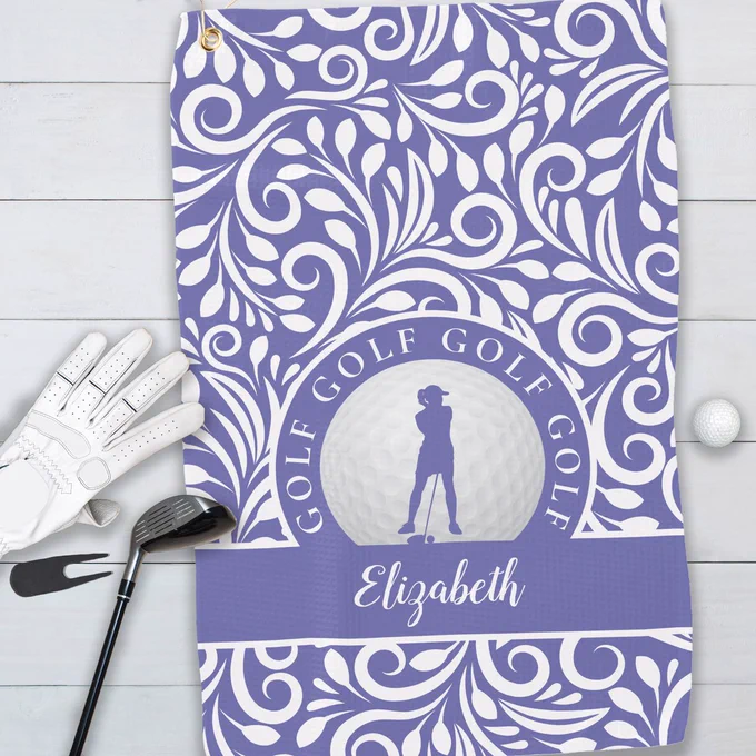 Custom golf towel featuring a female golfer silhouette on a realistic golf ball, set against a periwinkle blue background with modern swirls and leaves. Includes a customizable monogram space for a personalized touch. All colors in this design may be customized to match personal style or team colors.