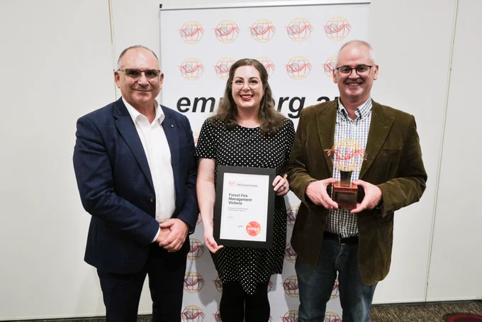 Three people stand smiling holding framed awards.