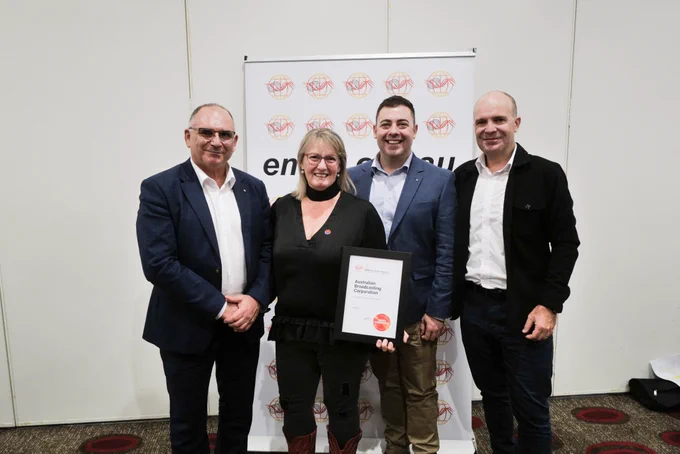Four people stand smiling holding a framed certificate.
