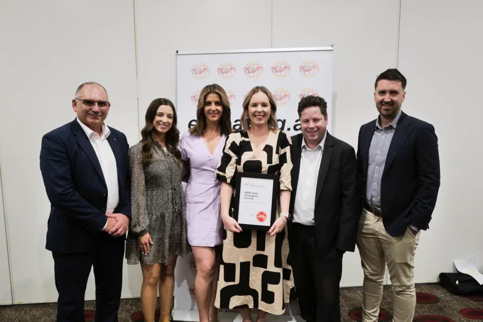 Six people stand together smiling as one holds a framed certificate.