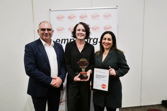 Two women hold a certificate and a trophy, next to a man.