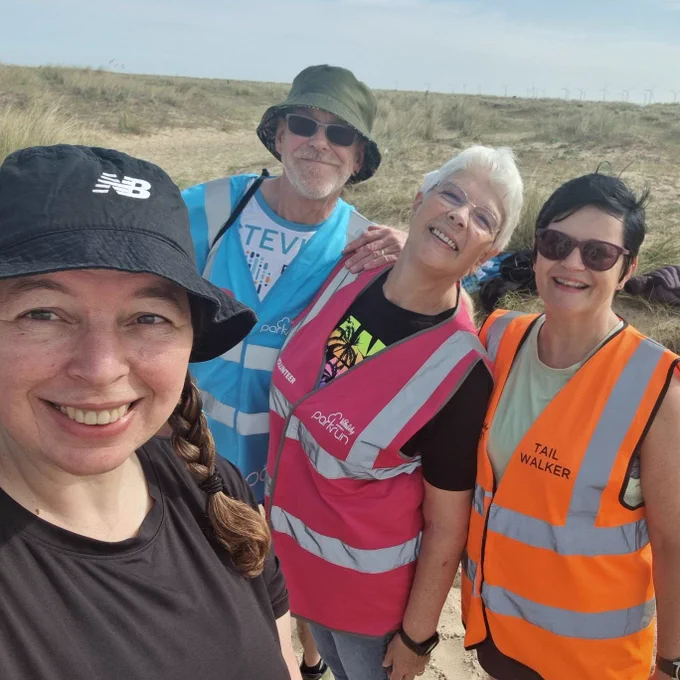 4 parkrunners, 3 of whom are wearing volunteer bibs, smiling for a selfie on the beach.
